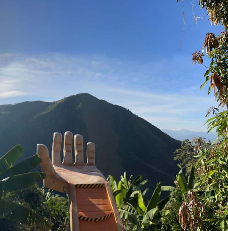 A carved wooden hand at a viewpoint over the green Antioquia mountains