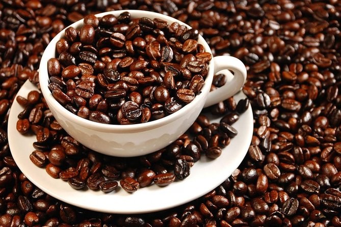 A cup and saucer sitting in a bed of dark roasted Colombian coffee beans